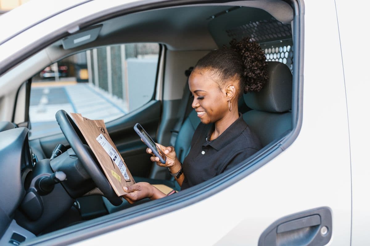 Kurierfahrerin am Steuer prüft eine Meldung auf dem Smartphone